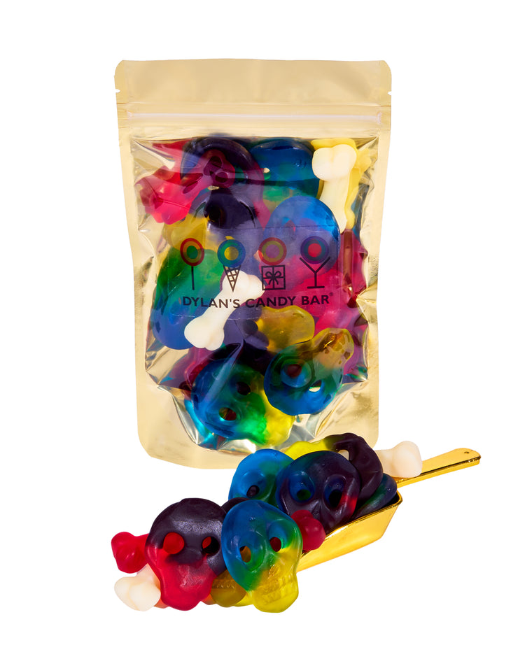 Fruity Gummy Skulls & Bones in resealable gold mylar bag next to Fruity Gummy Skulls & Bones overflowing from gold scoop